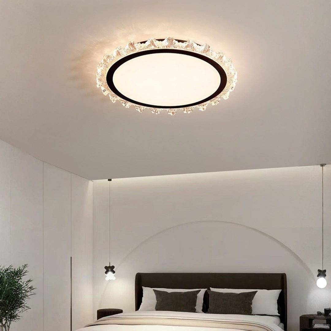 Modern white round led ceiling light with a black ring and crystal edge over a cozy bed space.