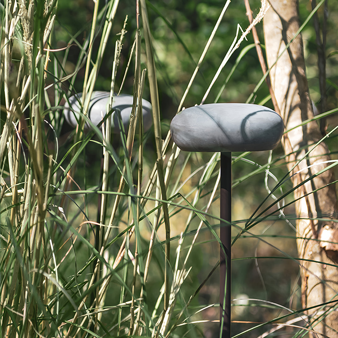 White mushroom pathway light surrounded by tall wild grass in a natural outdoor setting.