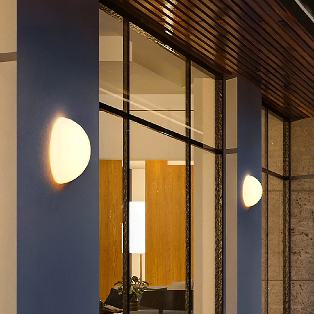 Warm outdoor lighting wall mounted fixtures installed near large glass windows at dusk.