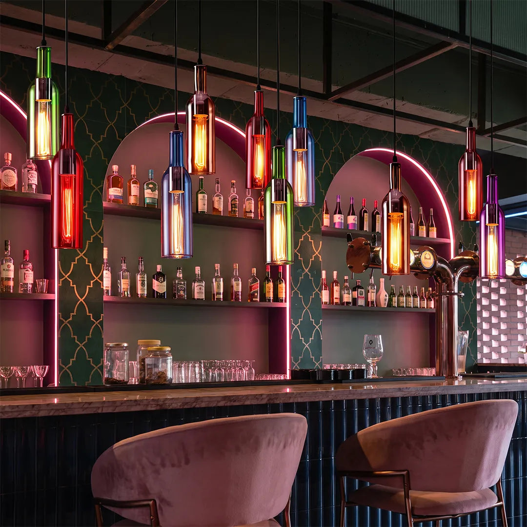 Wine bottle pendant lights hanging above a colorful lounge bar with neon accents and velvet chairs.