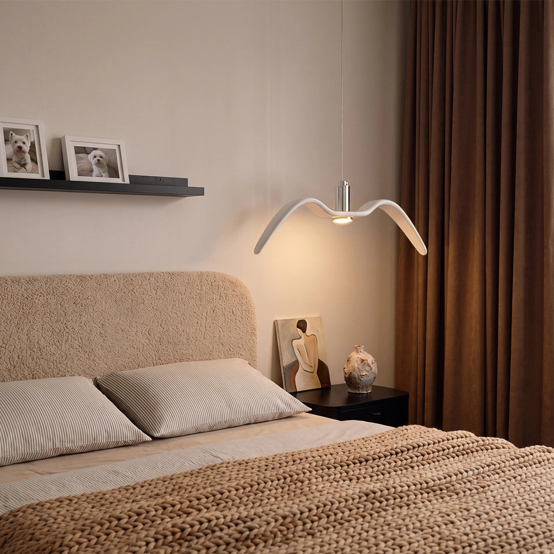 Wing pendant light glowing above a bed in a cozy bedroom with warm curtains and soft neutral decor.