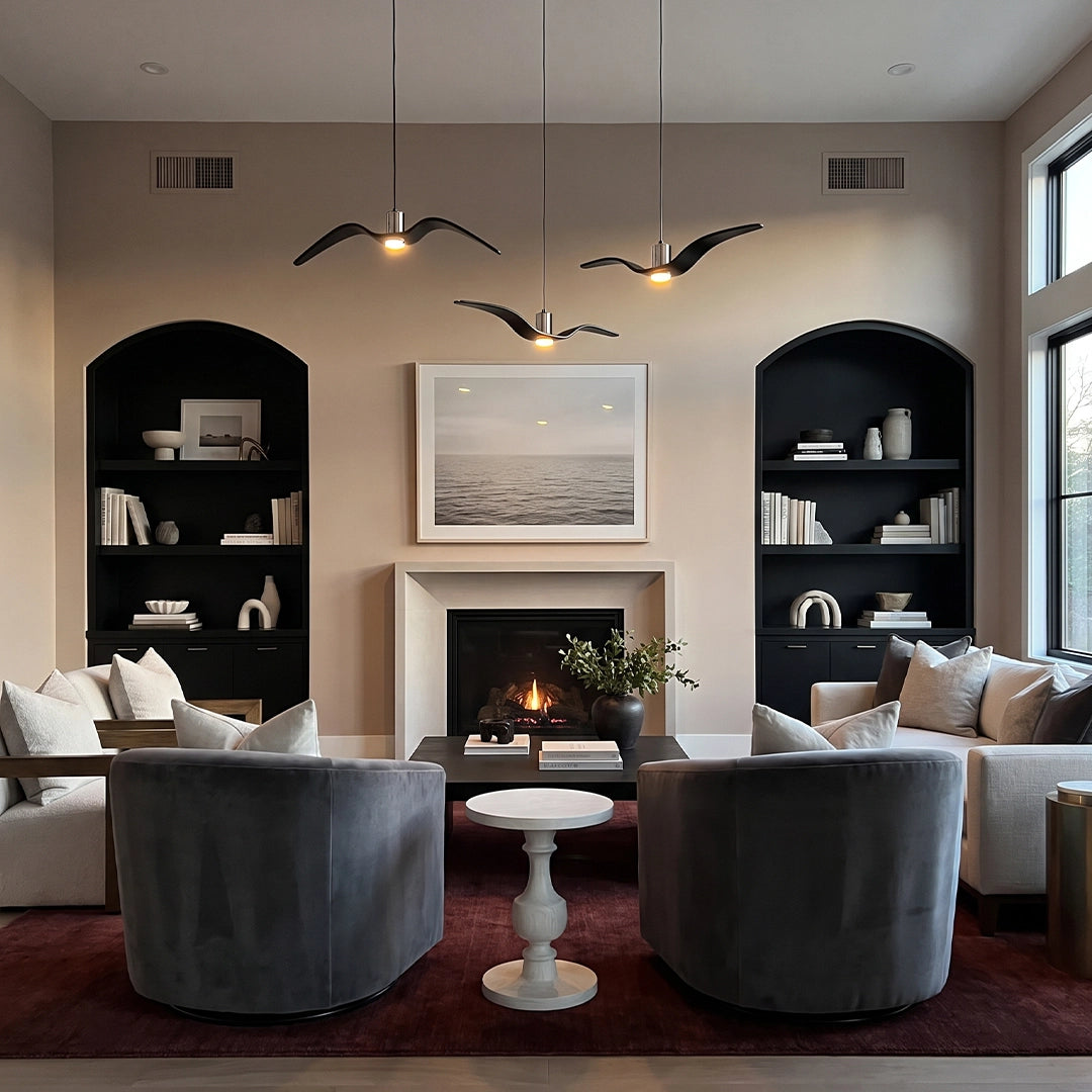 Wing pendant lights suspended in a living room with a fireplace, built-in shelves, and lounge chairs.