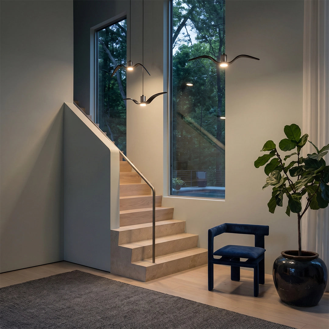 Wing pendant light hanging beside a staircase and window, adding warm light to a modern interior.