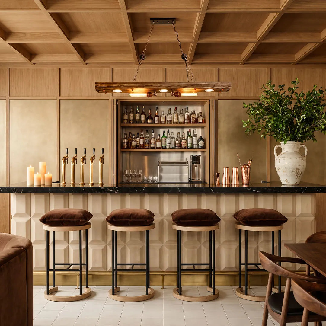 Wood and metal chandelier hanging above a home bar with a rustic beam and exposed bulb design.