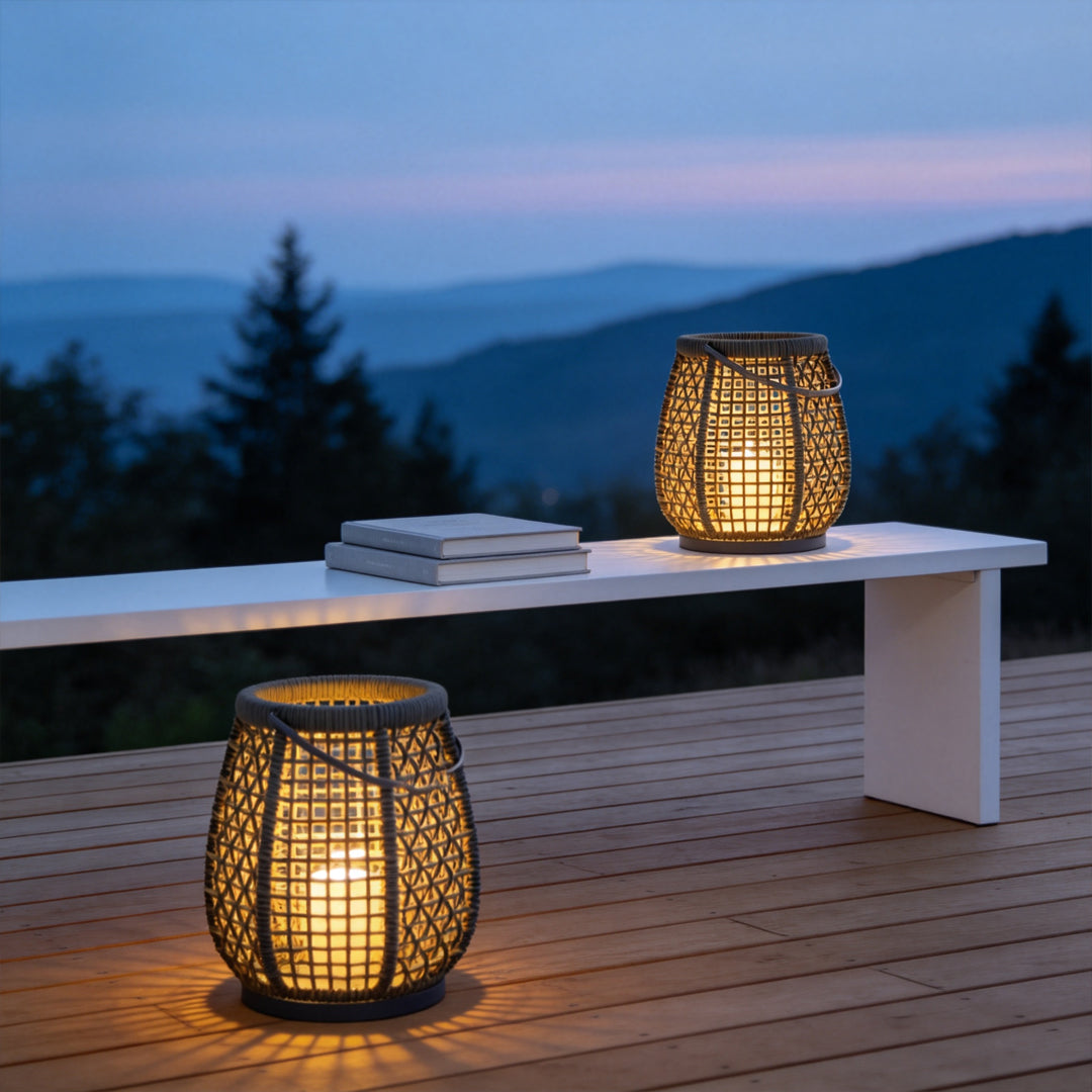 Woven outdoor lanterns placed on a wood deck at dusk, casting a warm glow beside a white bench with mountain views.