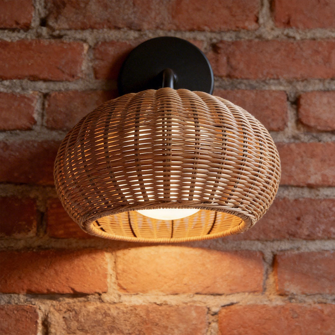 Woven rattan outdoor pendant light mounted as a wall sconce on a rustic red brick wall facade.