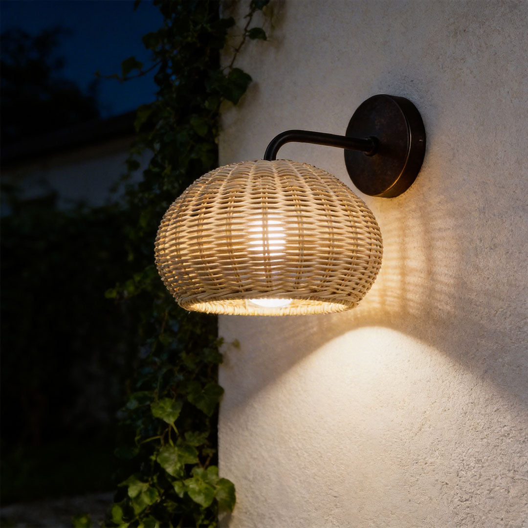Woven rattan outdoor pendant light mounted as a wall sconce on a textured beige plaster wall.