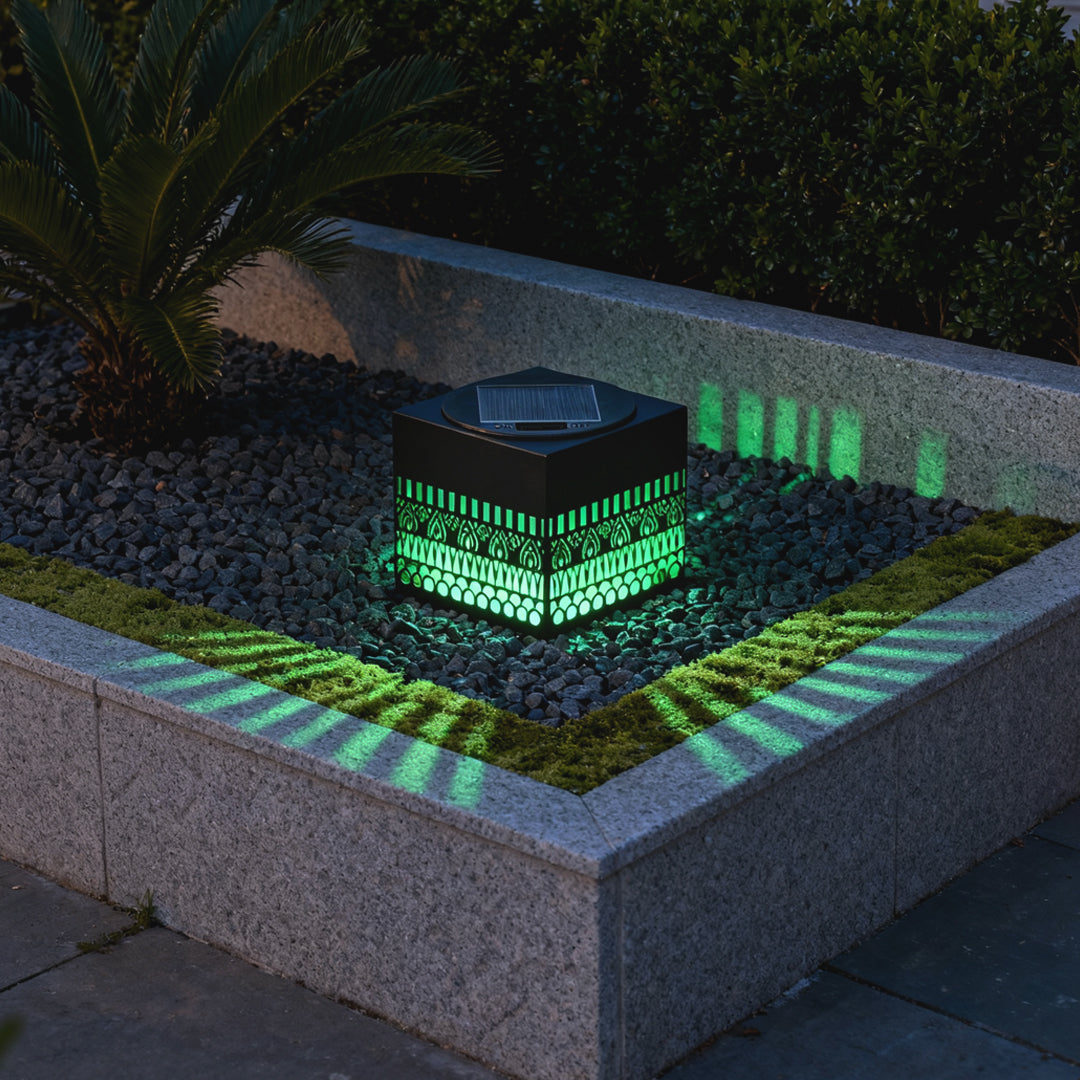 Outdoor garden bed lit by vivid LED colors reflecting around a decorative cube styled like wrought iron outdoor wall lights.