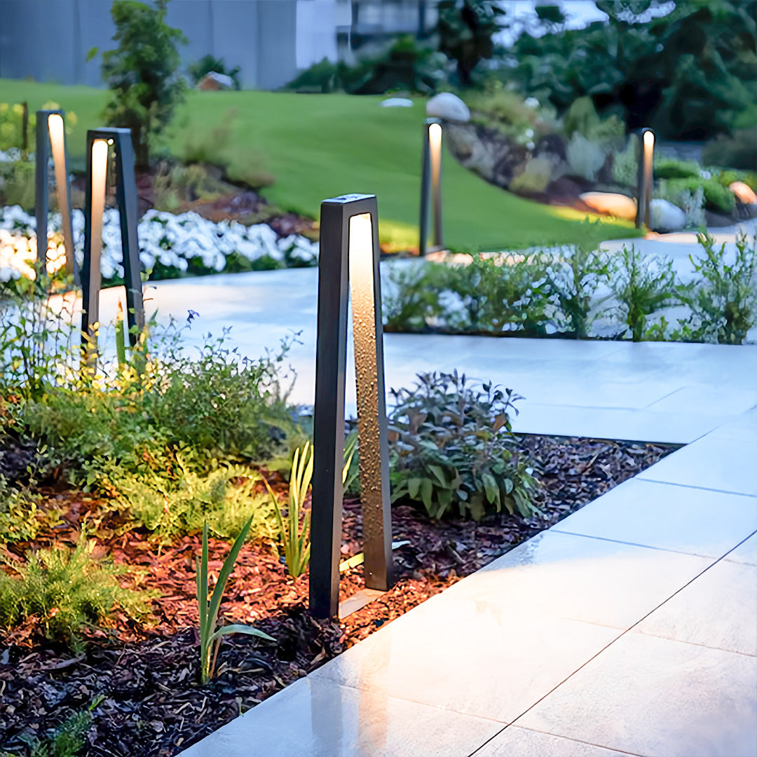 Contemporary bollard fixtures casting outdoor lighting for landscaping around a landscaped yard border.