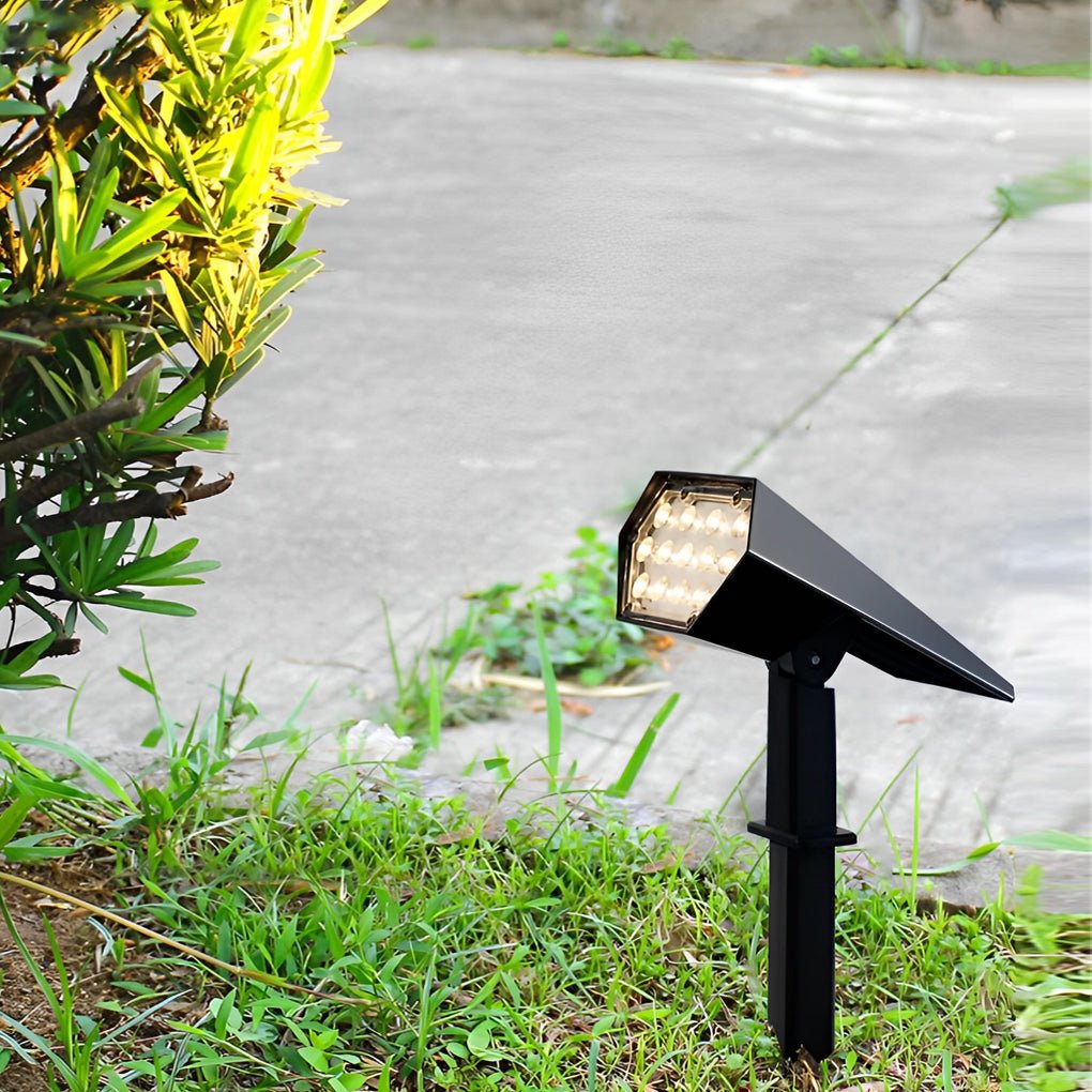 Flood spike light with adjustable solar panel shining on green bushes for energy-efficient landscape lighting.
