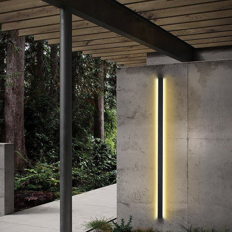 Long black outdoor lights providing ambient glow, mounted on a modern building beside a reflective pool.