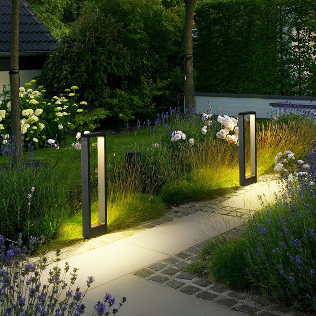 Black bollard lights illuminating a garden pathway with lush greenery and flowers.
