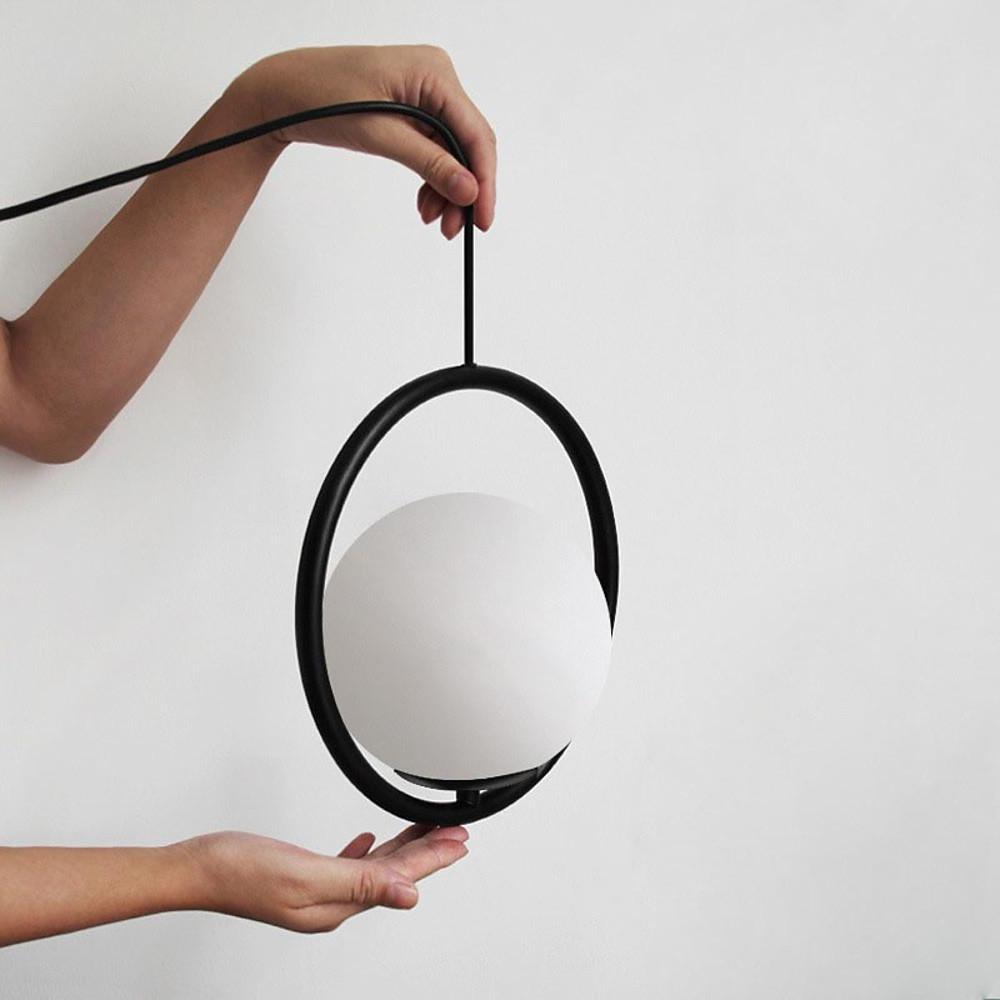 Hand holding a black circular pendant light to show the matte frame and opal glass details.