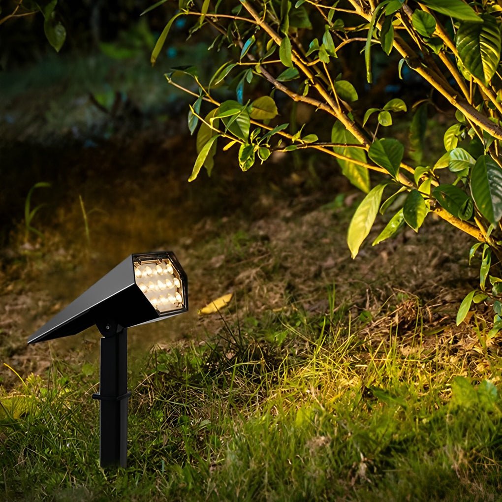 Black flood spike light in grassy area casting bright light on plants for enhanced garden visibility at night.