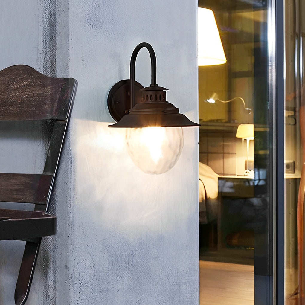 Black gooseneck wall light mounted beside outdoor seating area wall, classic industrial style exterior lighting fixture.
