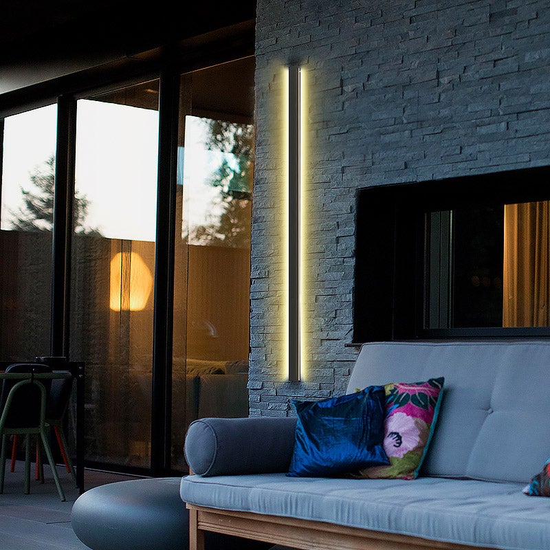 Black linear wall light illuminating a modern living room with elegant glow.