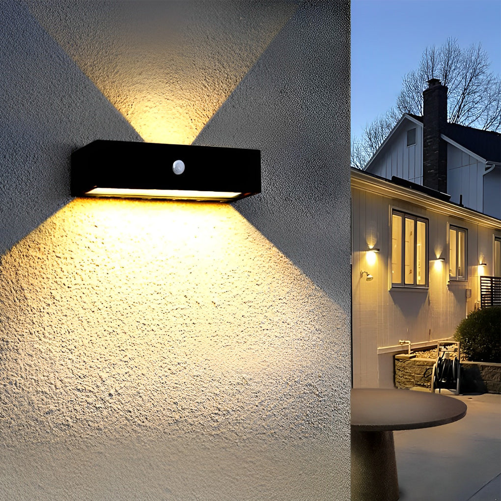 Black motion sensor outdoor wall light providing soft illumination along a stylish outdoor fence.