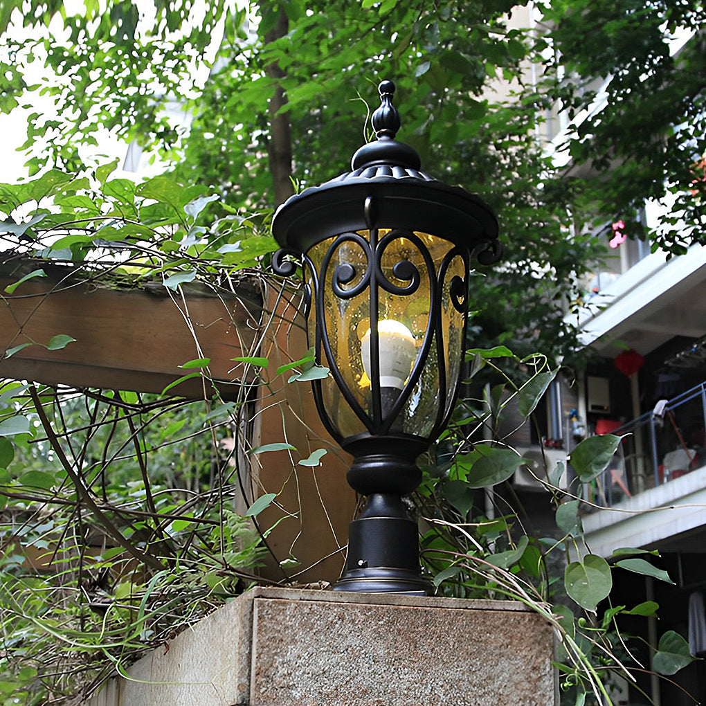 Black outdoor pillar light mounted on a wooden fence, providing ambient lighting in a garden.