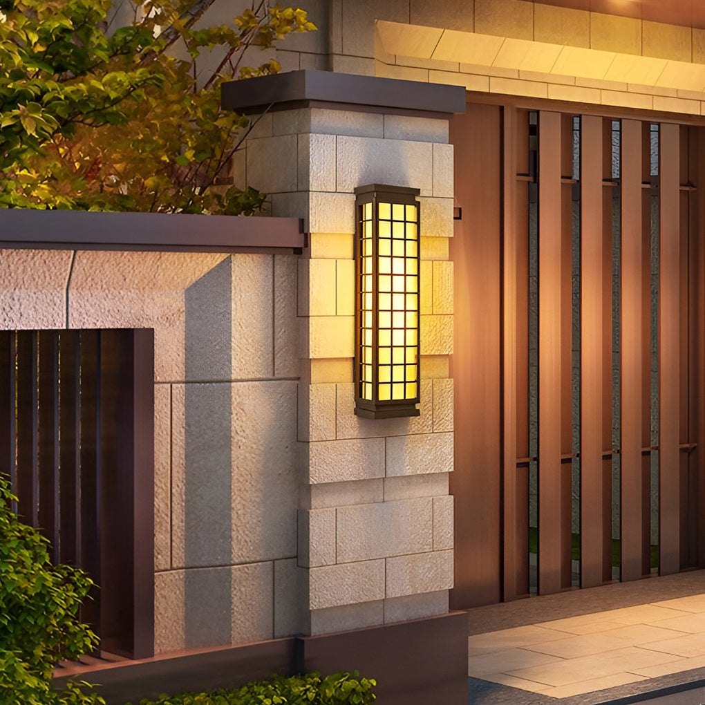 Black outdoor sconce light with grid pattern mounted on gray stone wall near wooden door.