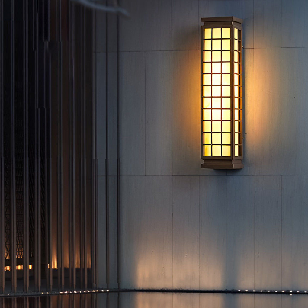 Black outdoor sconce light with grid design illuminating a modern wall and decorative statue.