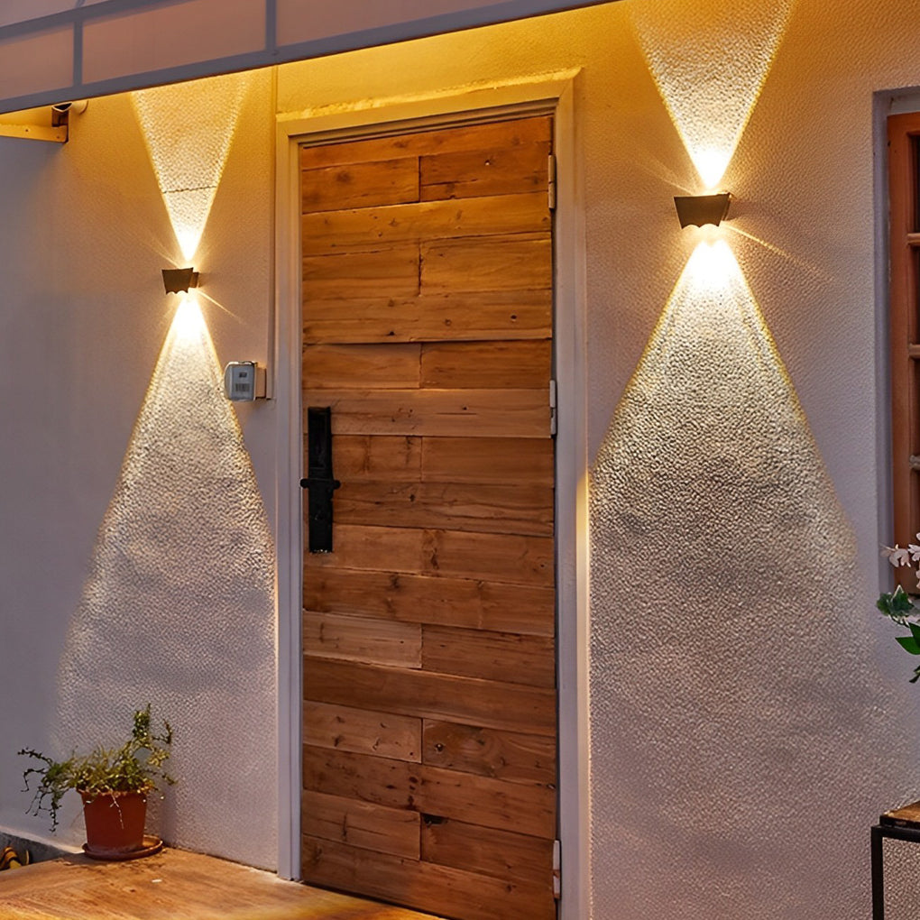 Black up down wall light beside a wooden front door, enhancing entryway lighting with a modern geometric glow.