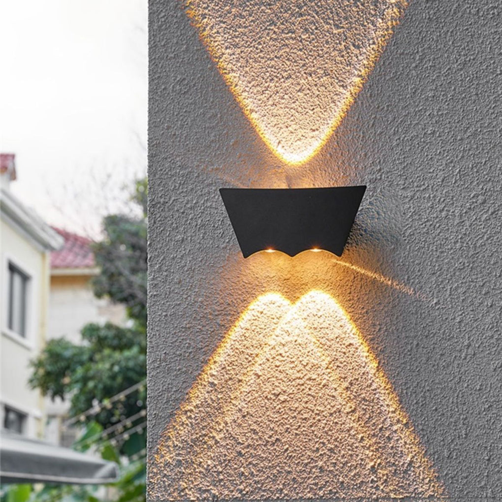 Black up down wall light illuminating an outdoor wall surface, creating dramatic X-shaped lighting effects at night.