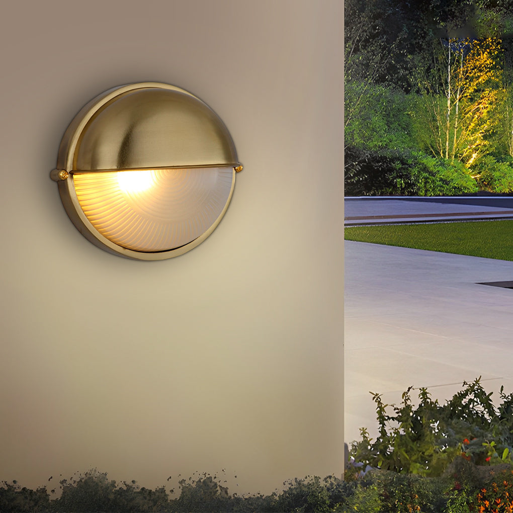 Brass-finished oval bulkhead light installed outdoors, creating a warm glow against a wall at night.