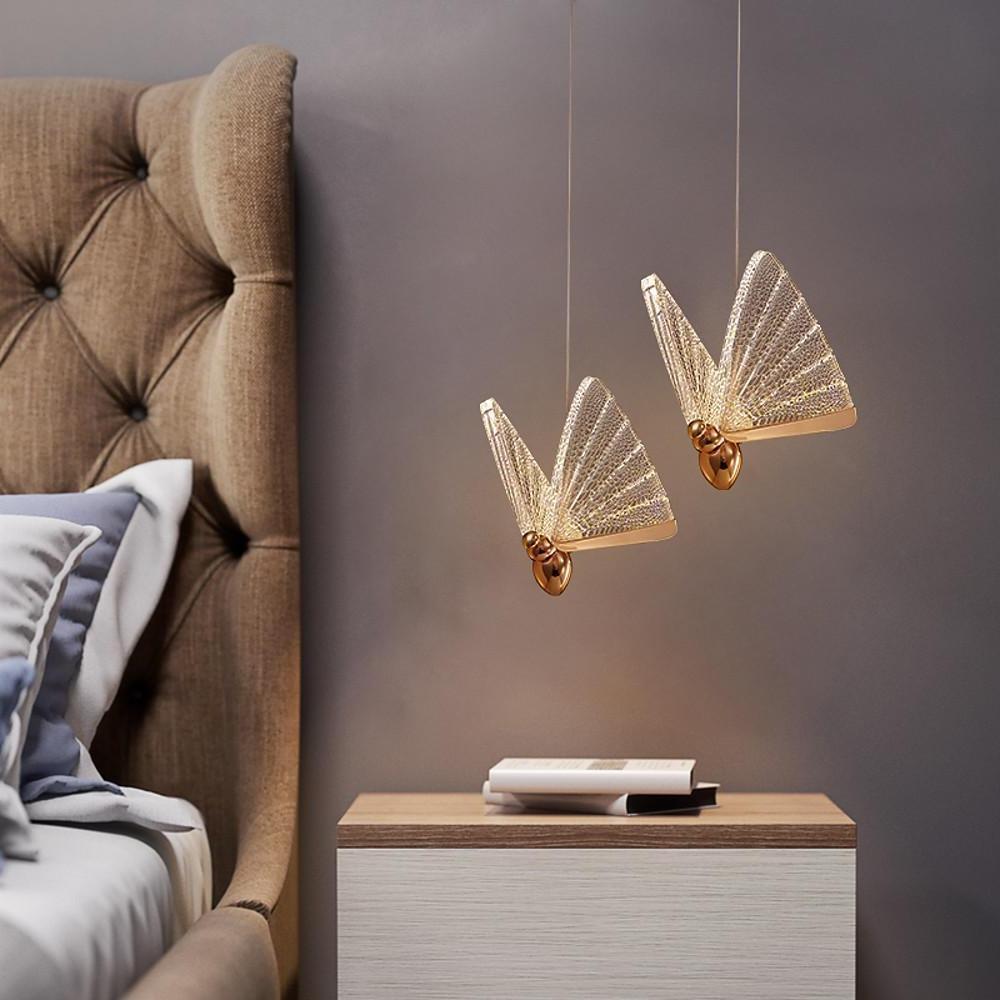 Modern butterfly pendant light hanging next to upholstered bed headboard.