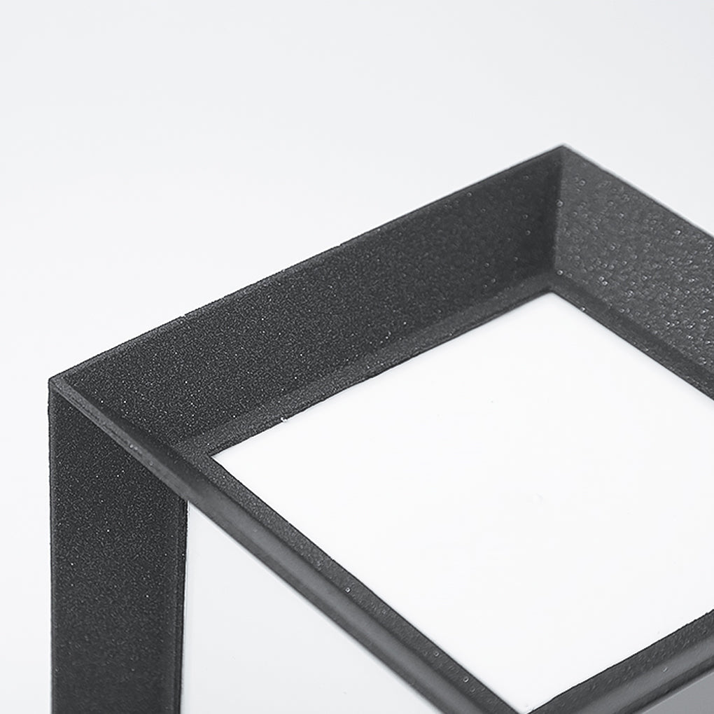 Close up detail of the top square frame on textured black outdoor bollard lights against white.