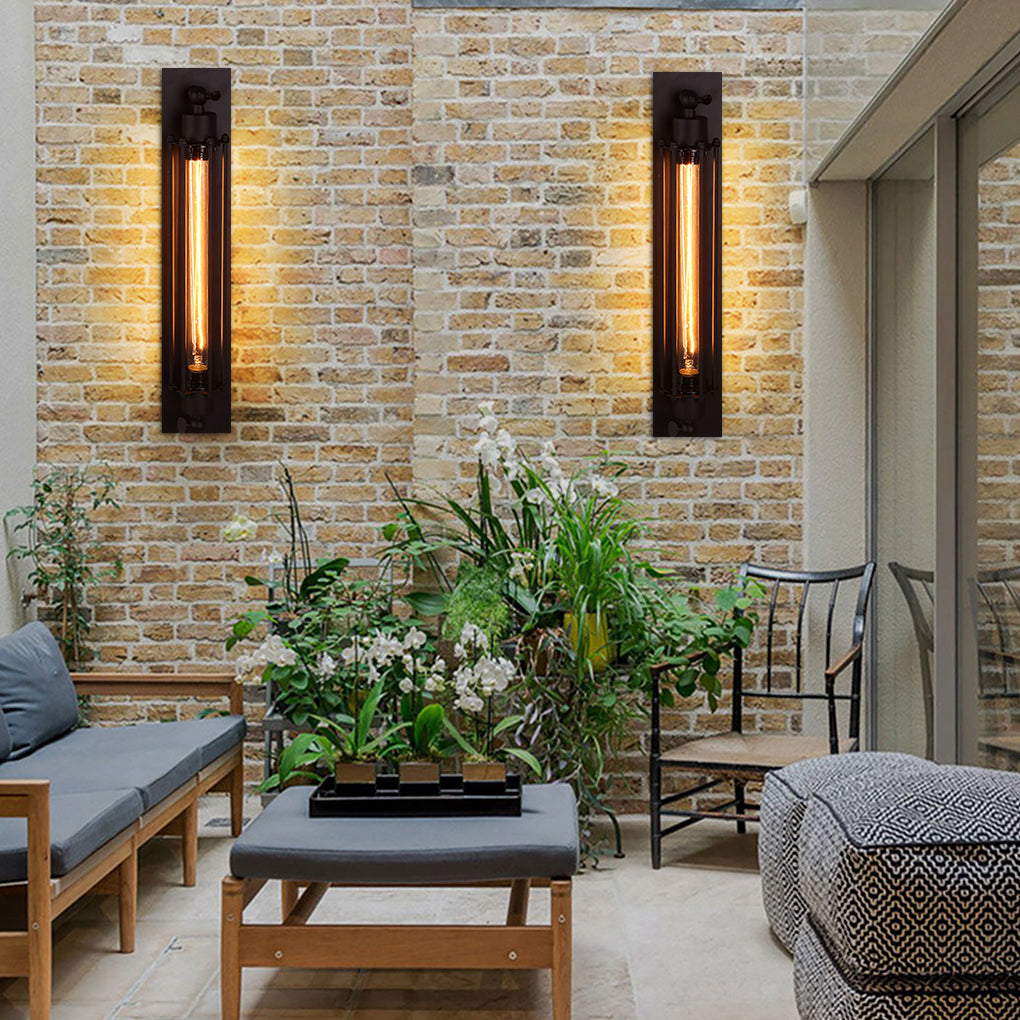 Vintage industrial wall sconce with elongated design, mounted on brick wall beside indoor plants for cozy lighting.