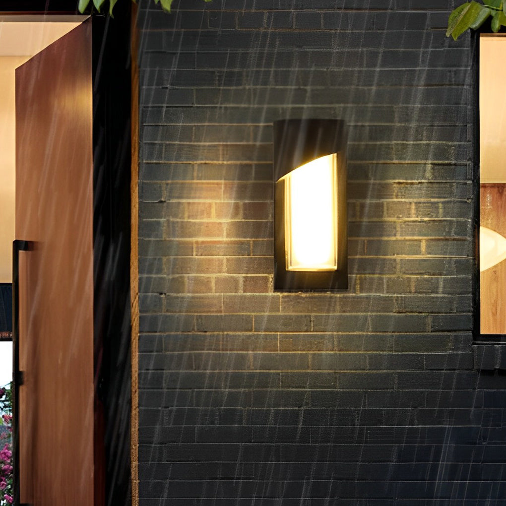 Black outdoor wall light with frosted panel on brick wall near garden.