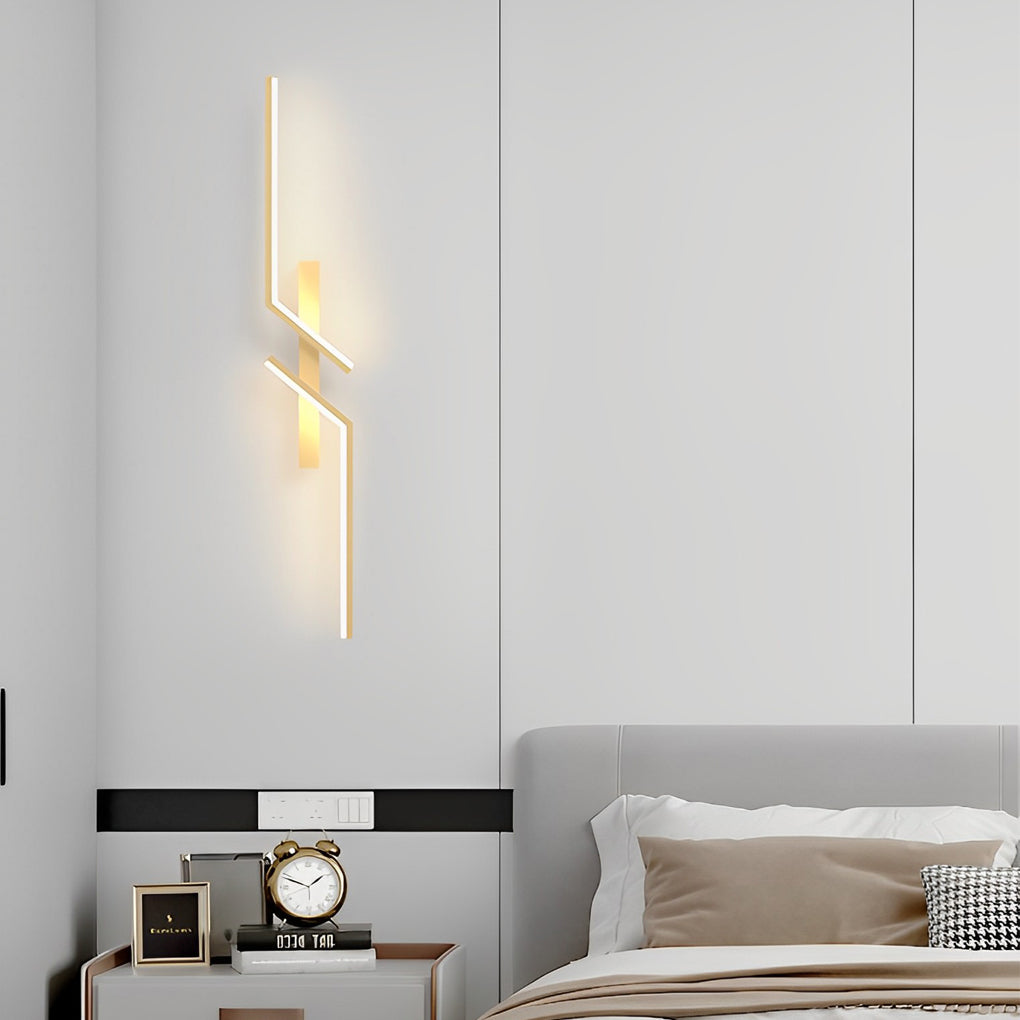 Geometric wall sconce with a gold finish, mounted beside a bed with modern decor.