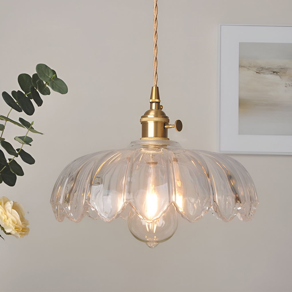 Clear glass pendant light with flower-shaped shade and brass hardware, emitting warm light in a modern interior.