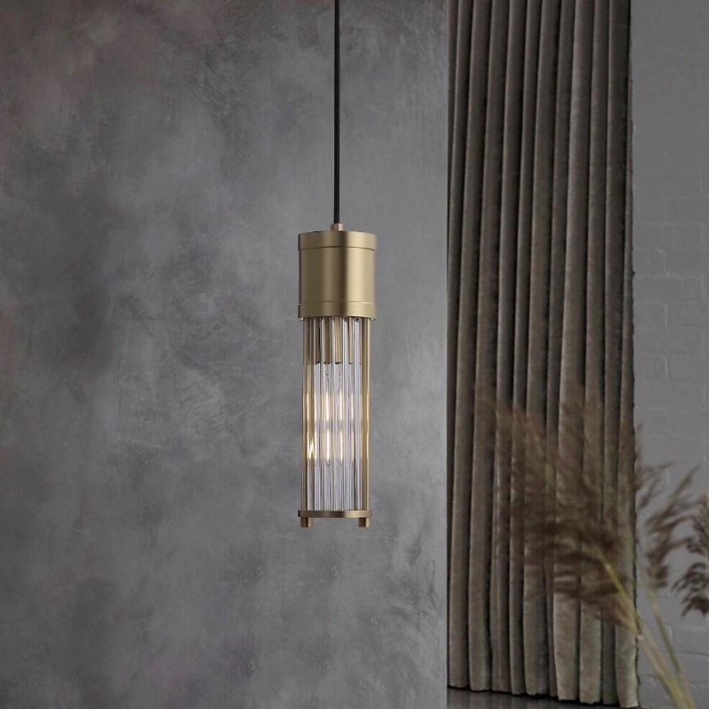 Gold cylinder pendant light suspended in minimalist interior setting.