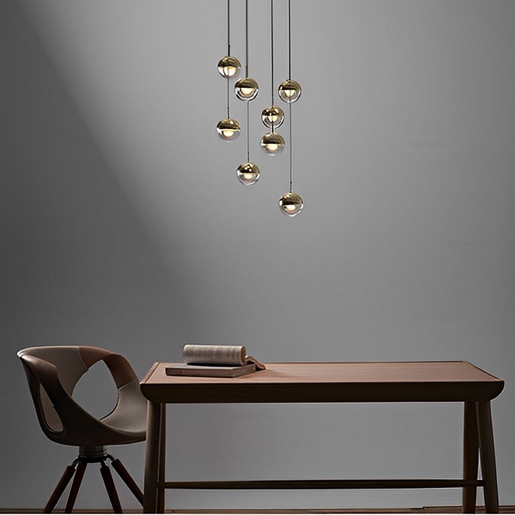 Cluster of gold globe pendant light fixtures hanging over a wooden desk in a minimalist room.