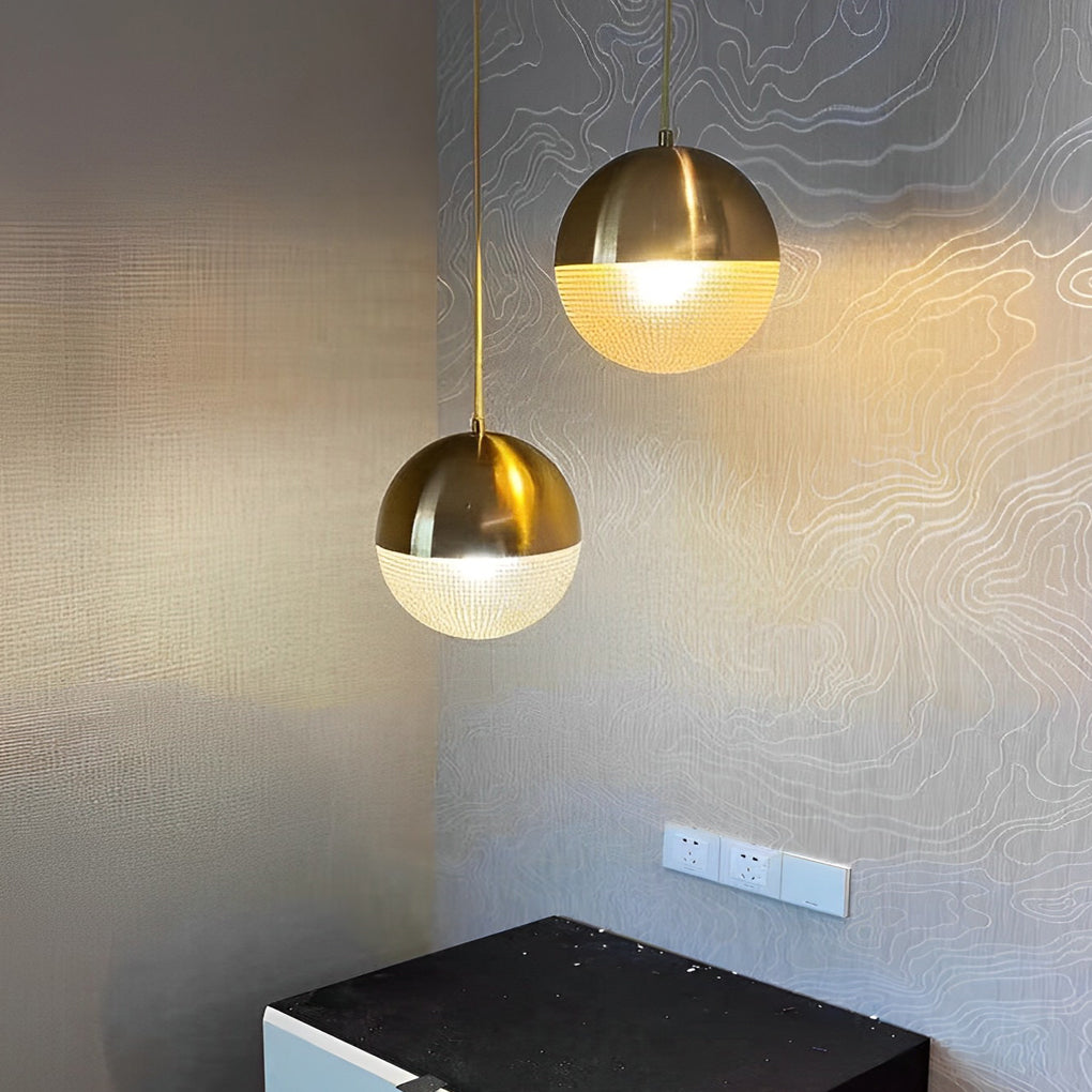 Pair of gold globe pendant light fixtures reflecting light on a textured silver accent wall.