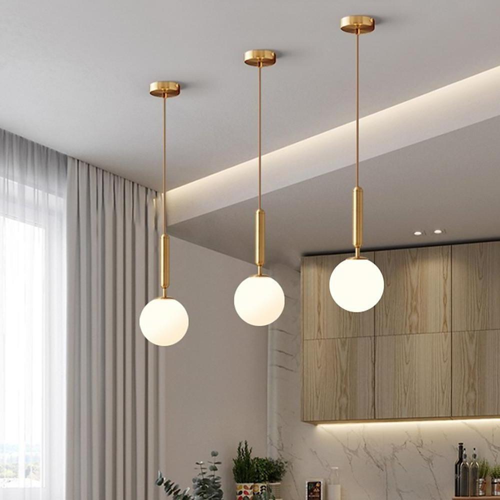 Trio of gold hanging lights installed in a row over a modern dining table with wooden cabinetry.