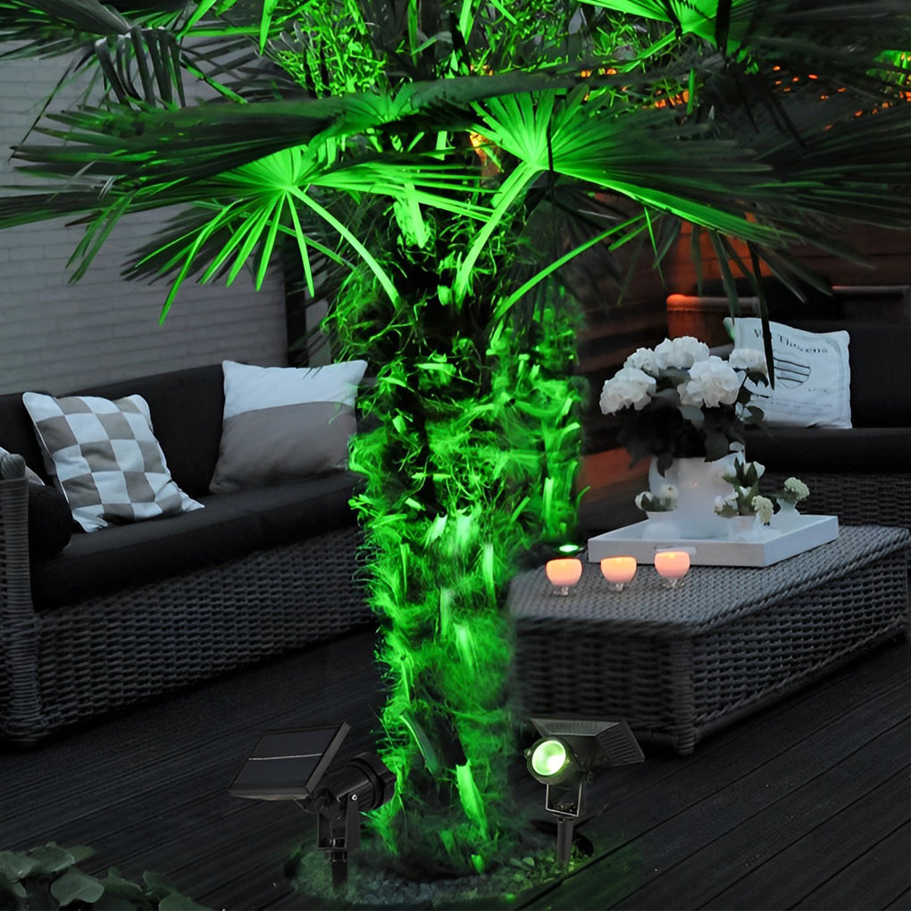 Green ground spike solar lights illuminating a palm tree trunk beside a modern patio seating area.