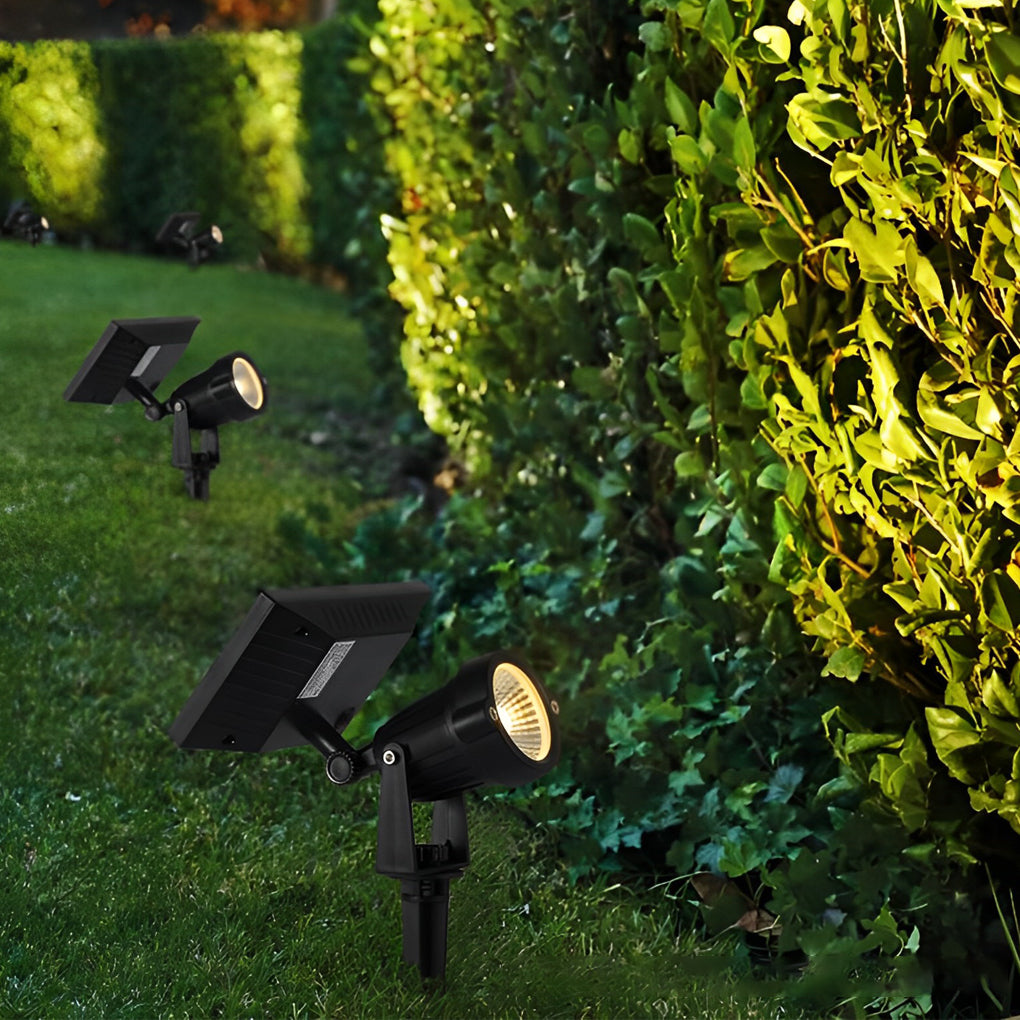 Ground spike solar lights installed along a hedge, providing directional accent lighting for garden borders.