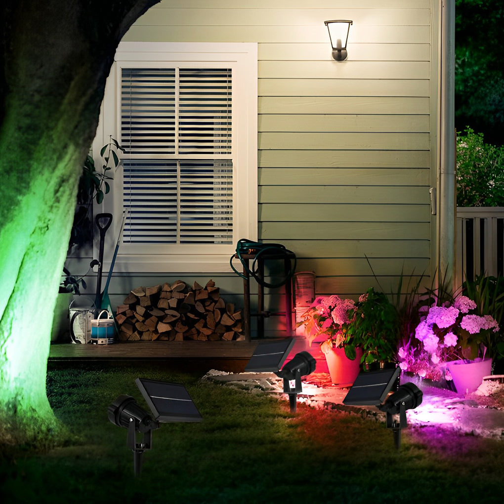 Ground spike solar lights illuminating a house exterior, garden plants, and lawn for nighttime curb appeal.
