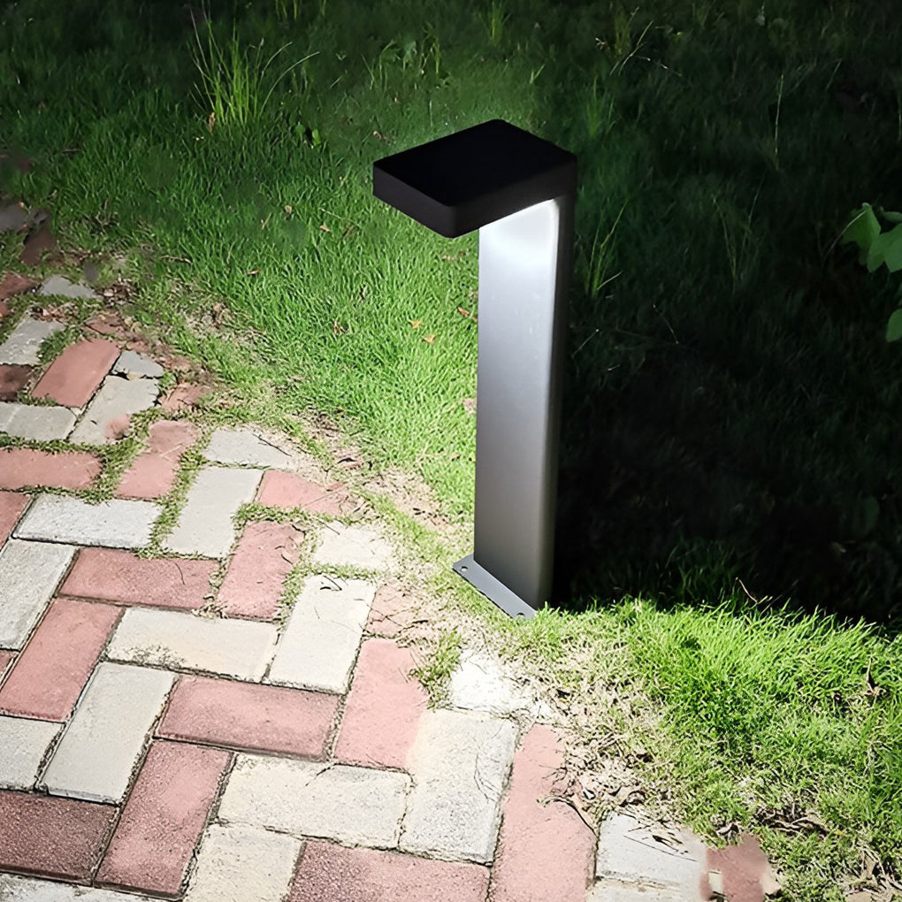 L shaped landscape light with a sleek design, casting warm light on a brick pathway.