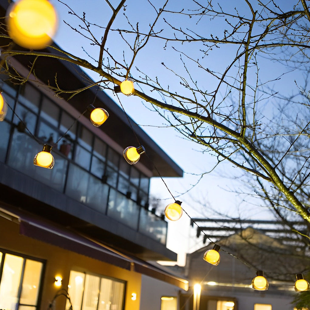 LED globe string lights stretched under a shade sail, enhancing a modern outdoor seating area with soft illumination.