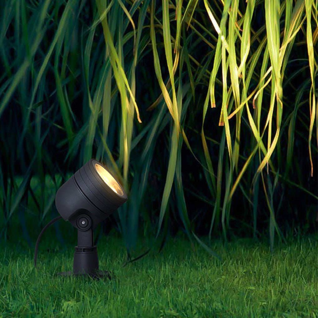 Compact LED landscape spot lights placed in grass, illuminating tall ornamental plants with directional outdoor lighting.