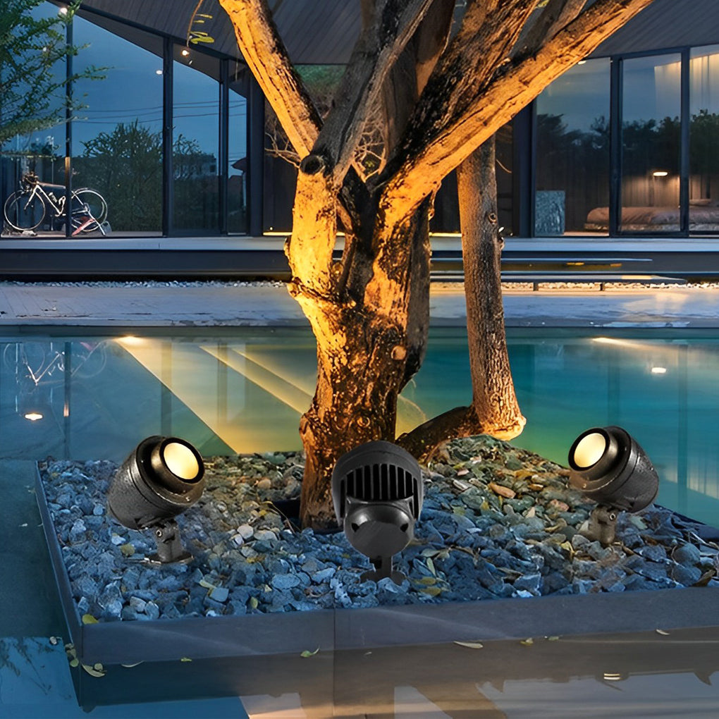 LED landscape spotlight illuminating tree roots beside a swimming pool area.