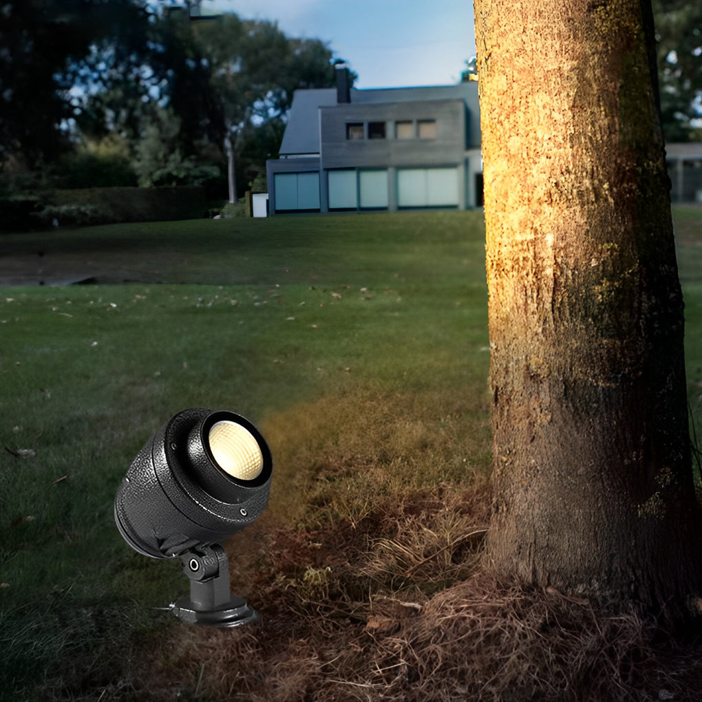 LED landscape spotlight focused on a single tree trunk in a residential lawn at night.