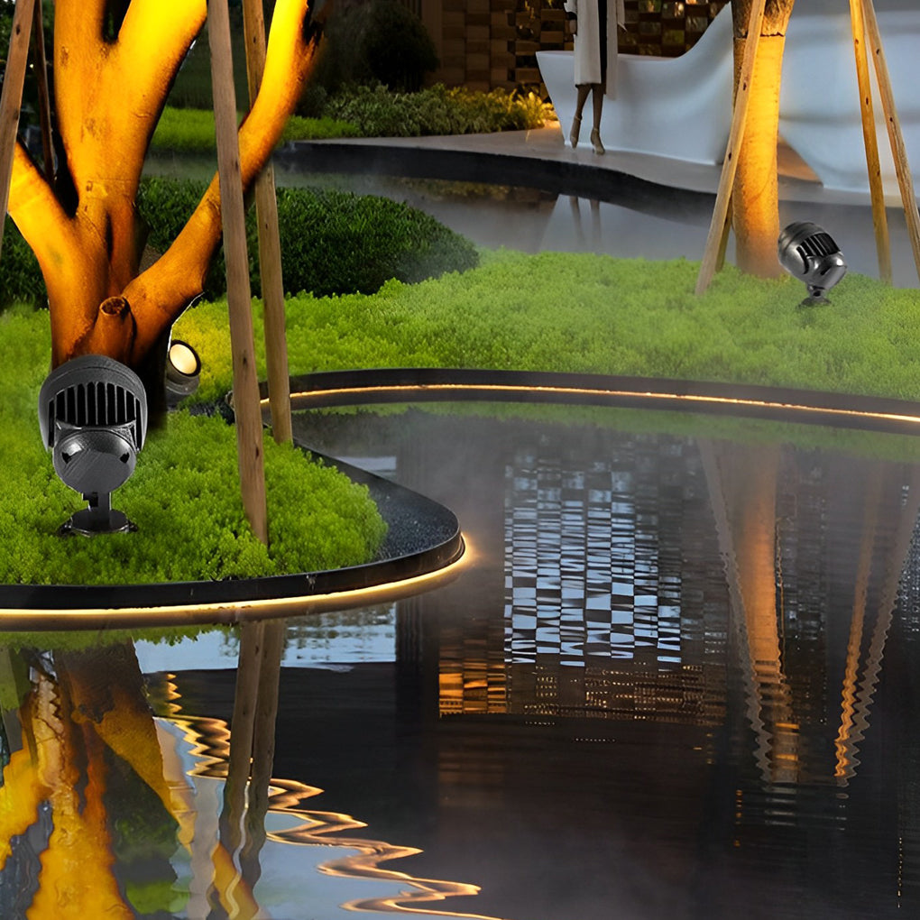 LED landscape spotlight reflecting warm light around trees near a water feature.