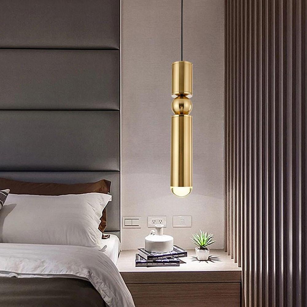 Luxurious gold cylinder pendant light with a sphere accent over a nightstand in a cozy bedroom.