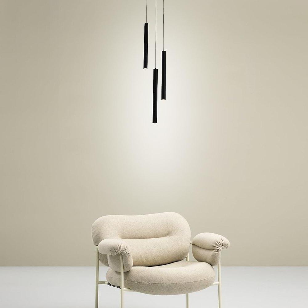 Minimalist black linear cluster pendant light trio staggered above a cozy cream bouclé chair.
