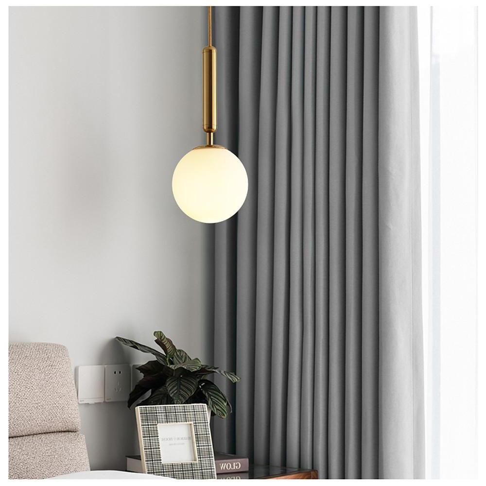 Minimalist frosted globe pendant light adding a soft glow next to a cozy bedroom bedside table.