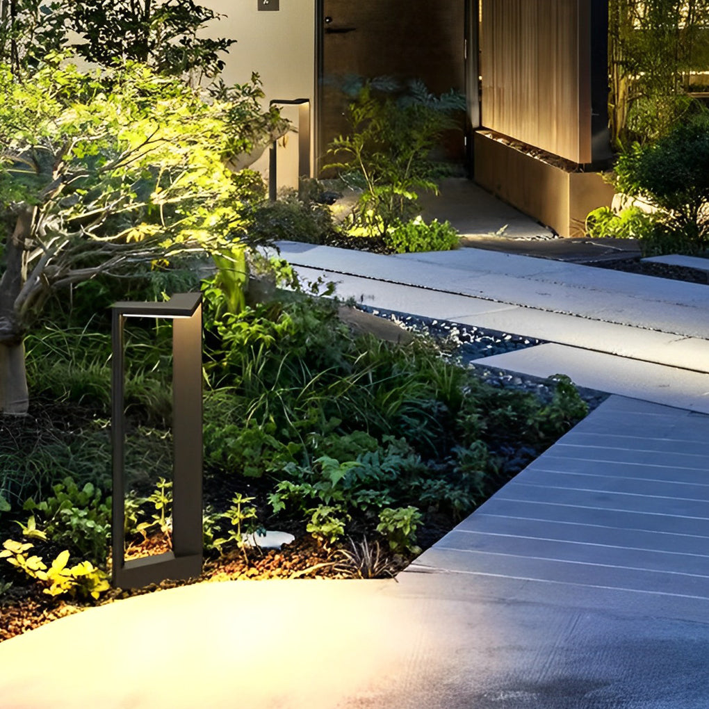 Modern architectural garden path light illuminating a concrete walkway near bright green trees.